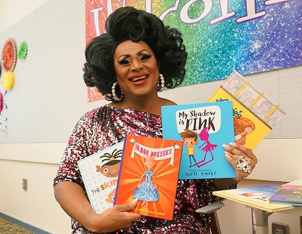 Drag queen Poison Waters smiling at the camera with four books in her hands.