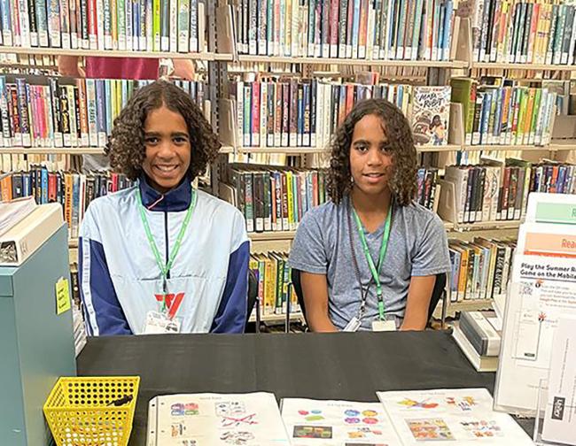 A set of twin volunteers seated at a Summer Reading table in the library