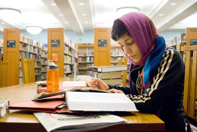 "Una persona estudiando en una mesa con  libros abiertos en una biblioteca"
